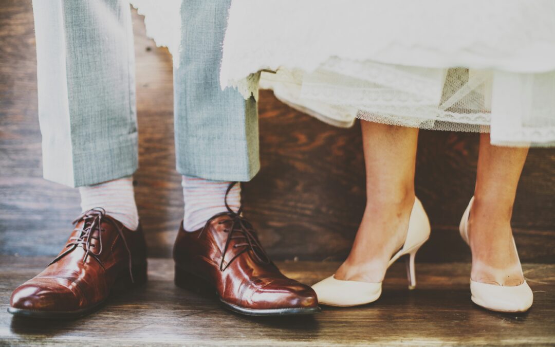 Photo of groom and bride from the knees down, showing suit pants and shoes and a wedding dress and high heels